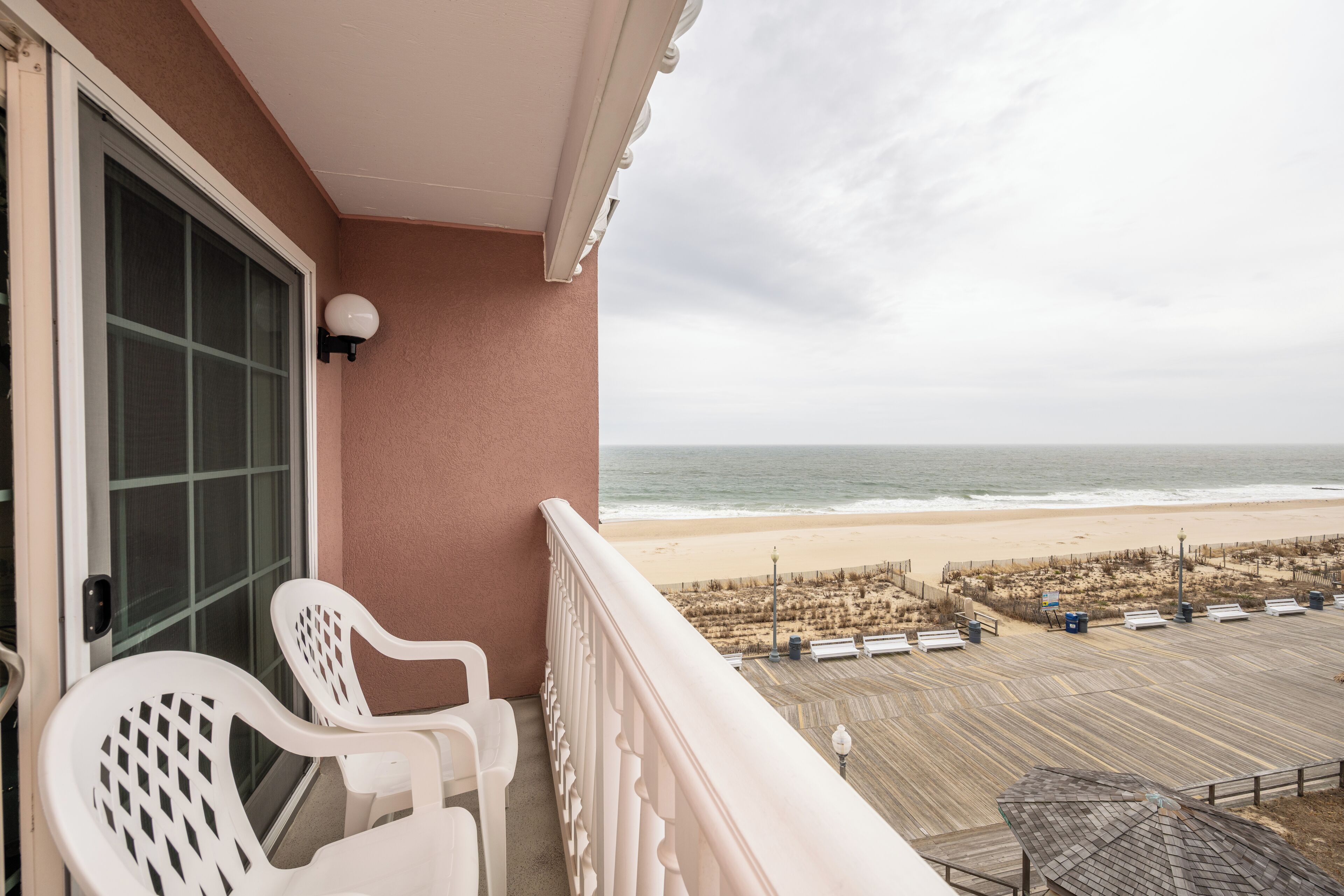 Ein Balkon mit weißen Stühlen, Blick auf den Strand und eine Holzterrasse.