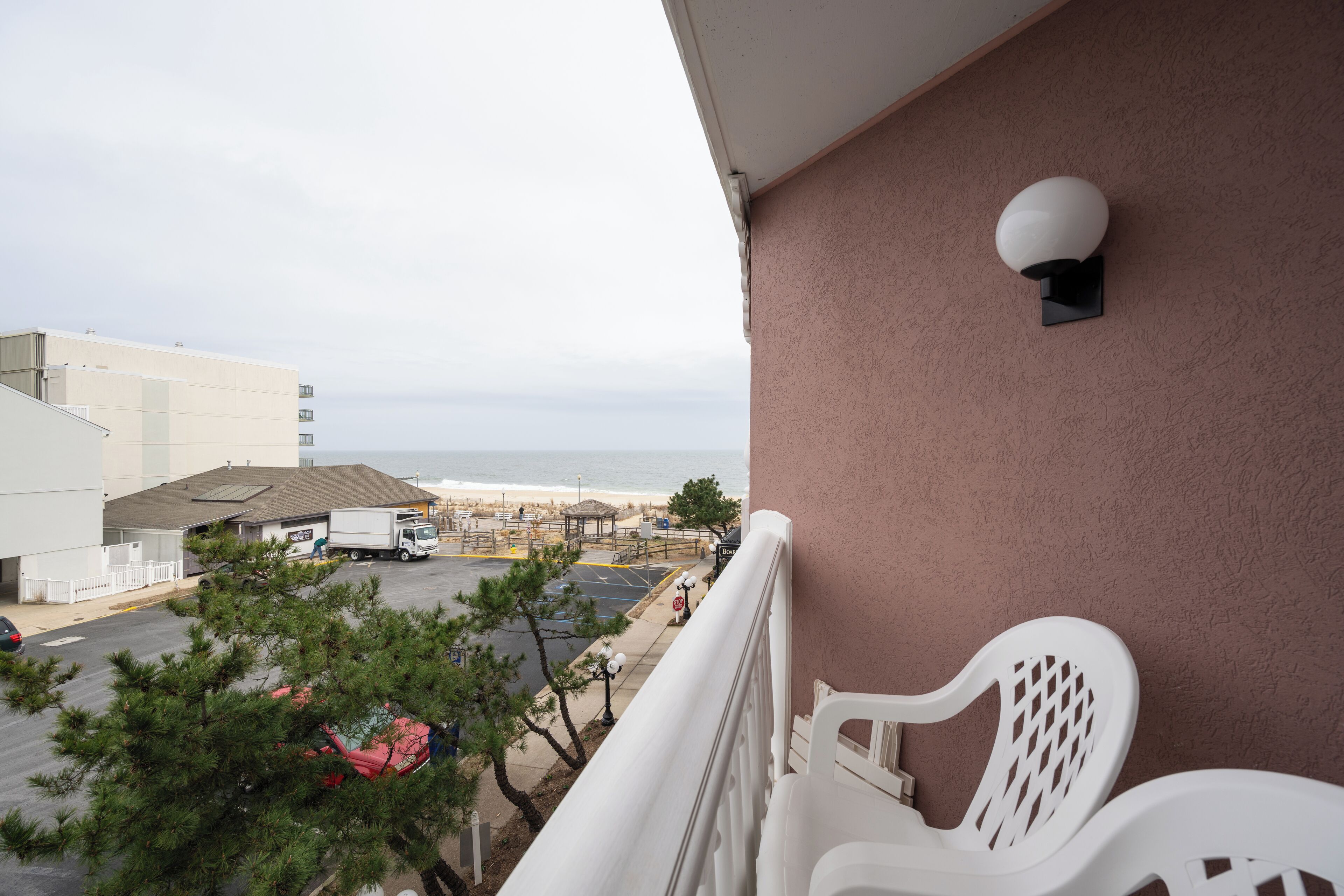 A balcony with a view of the beach and parking area.