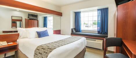 A hotel room with a large bed, a desk, a chair, a TV, a window with curtains, and a mirror.