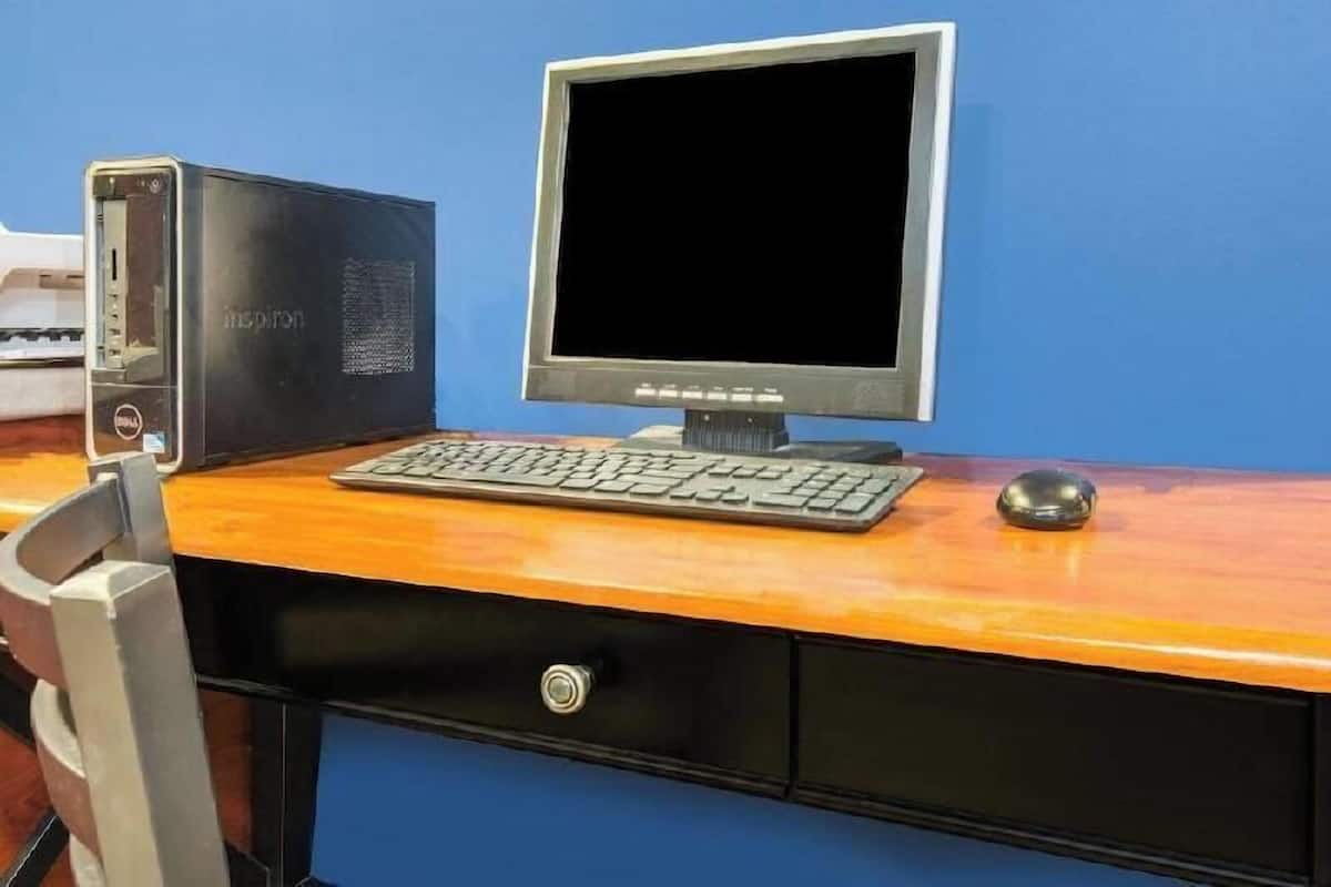 A desktop computer with a monitor, keyboard, and mouse on a wooden desk against a blue wall.