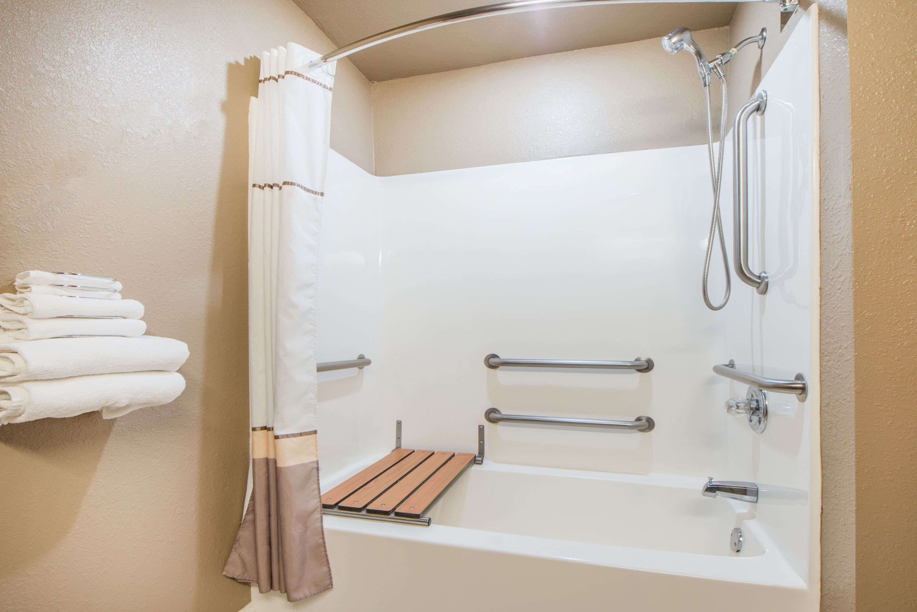 A modern bathroom with a bathtub, shower, and handrails.