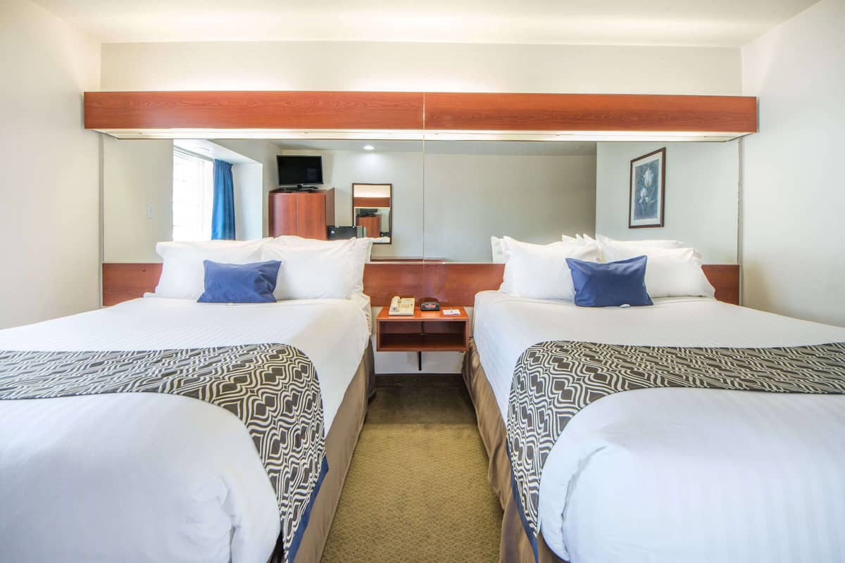A hotel room with two beds, a wooden headboard, a nightstand with a phone, and a mirror.
