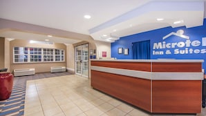 A reception area with a wooden reception desk, a blue wall with the Microtel Inn & Suites logo, a large window, and a red vase. - Microtel Inn & Suites by Wyndham Miami (Miami)