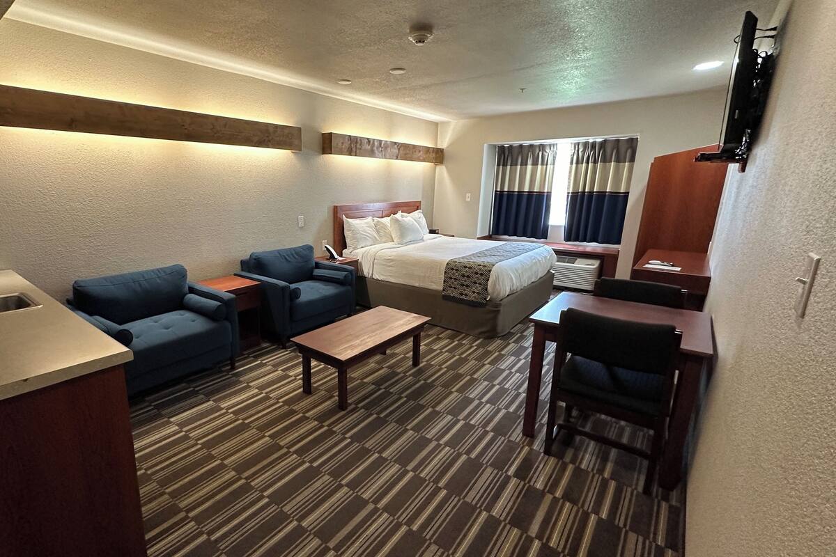 A compact hotel room with a kitchenette, a bed, a sofa, a small table, and a desk.
