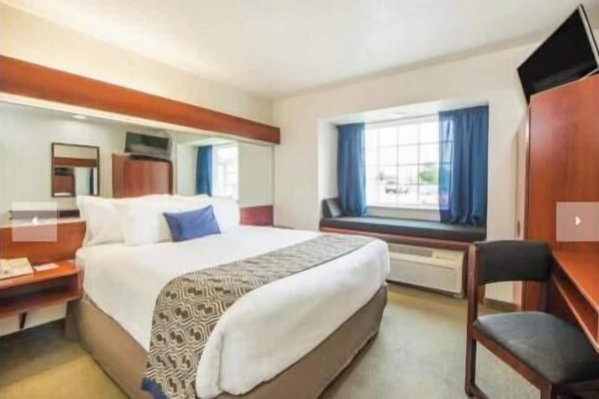 A hotel room with a large bed, a desk, a chair, and a window with curtains.