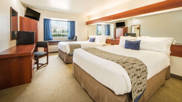 A hotel room with two beds, a desk, a chair, a TV, and a large window with curtains. - Microtel Inn & Suites by Wyndham Miami (Miami)