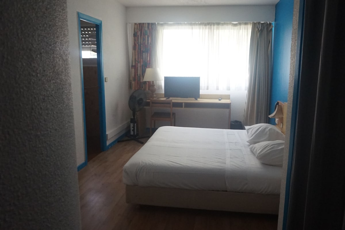 A hotel room with a bed, a desk, a chair, a television, and a window with curtains.