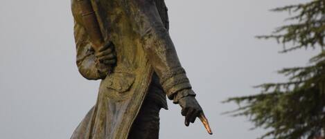 A statue of a historical figure holding a rifle, standing on a pedestal with a balustrade in the background.