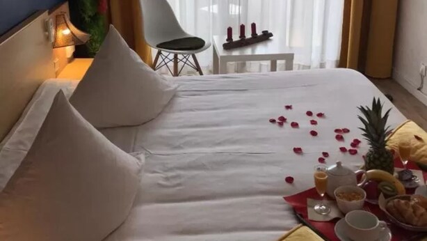 Una habitación de hotel con cama, una mesita con velas, una silla y una ventana con cortinas.