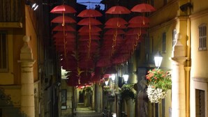 Una calle estrecha flanqueada por edificios, una persona caminando por ella, y sombrillas rojas colgadas del techo.