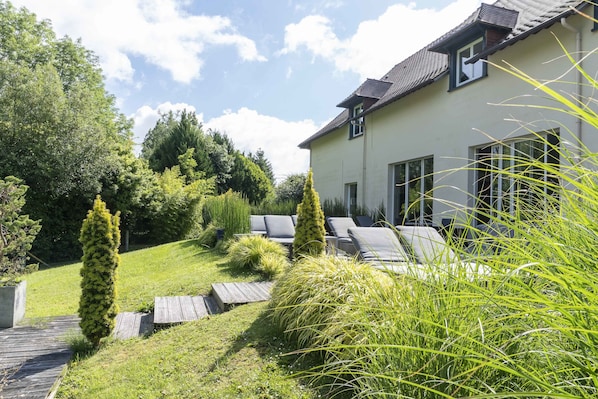 A modern house with a well-maintained garden, a wooden deck, and a seating area with outdoor furniture.