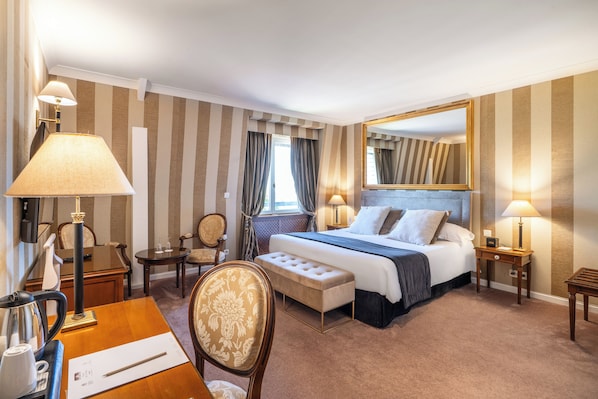 Habitación de hotel con una cama grande, mesitas de noche con lámparas, un escritorio con una silla, una pequeña mesa con una silla y un espejo grande en la pared.