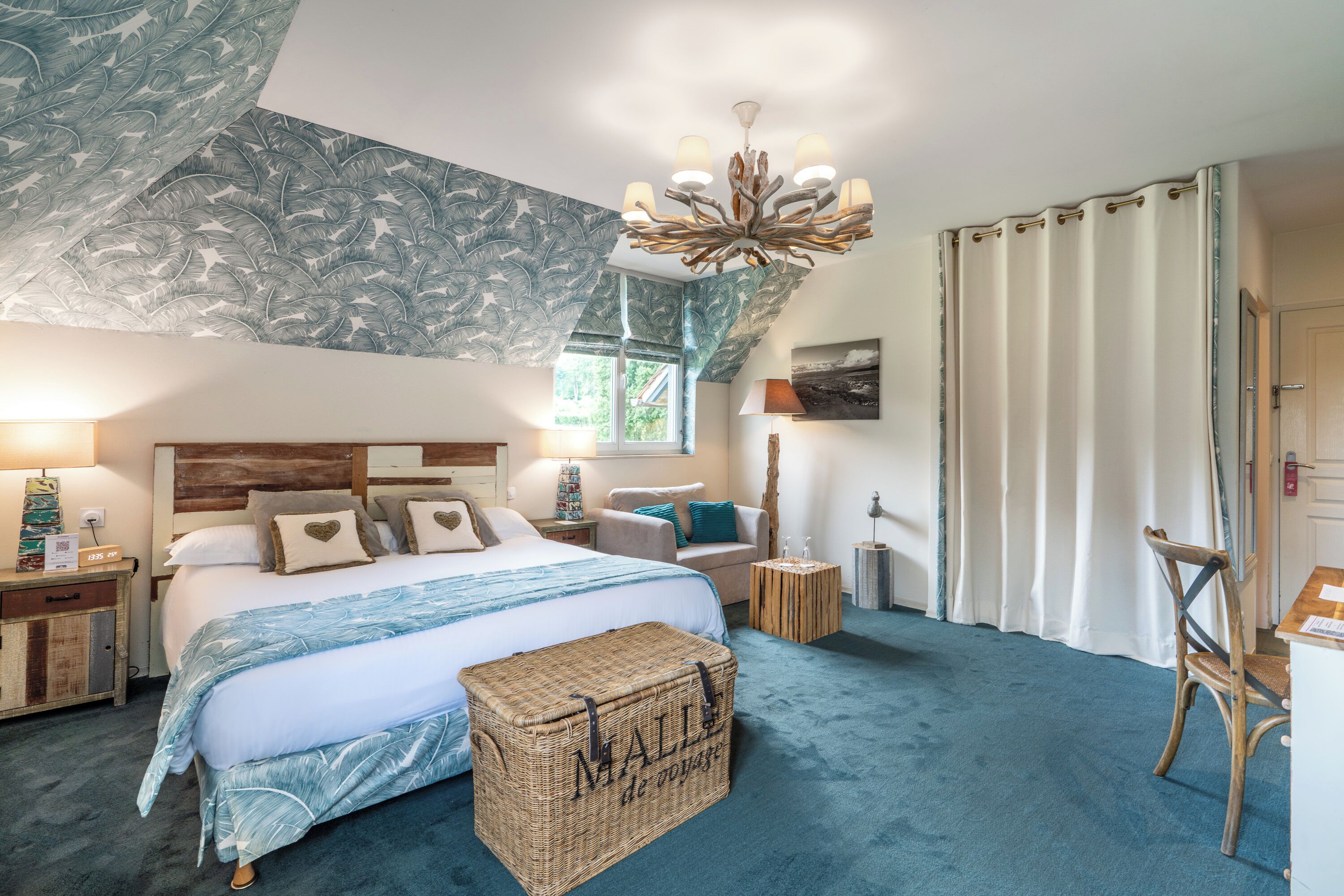 Une chambre à coucher avec un grand lit, une tête de lit en bois, un lustre, une fenêtre et une vue sur l’extérieur.