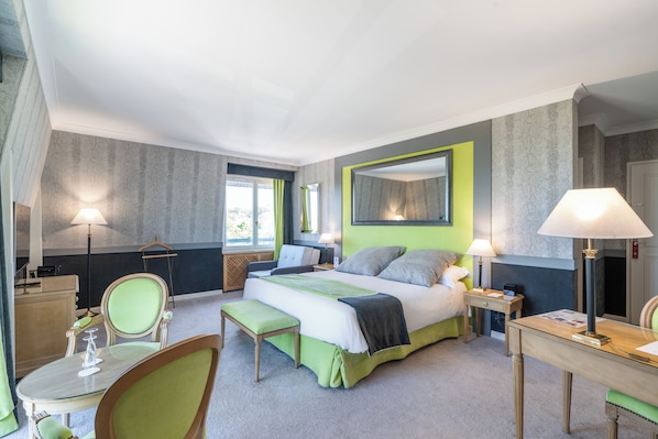 A hotel room with a large bed, bedside tables, a desk, a chair, and a bench.