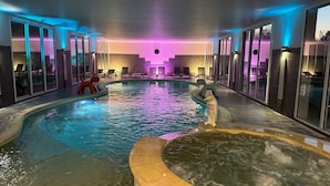 An indoor swimming pool with clear water, lounge chairs, and a jacuzzi area.