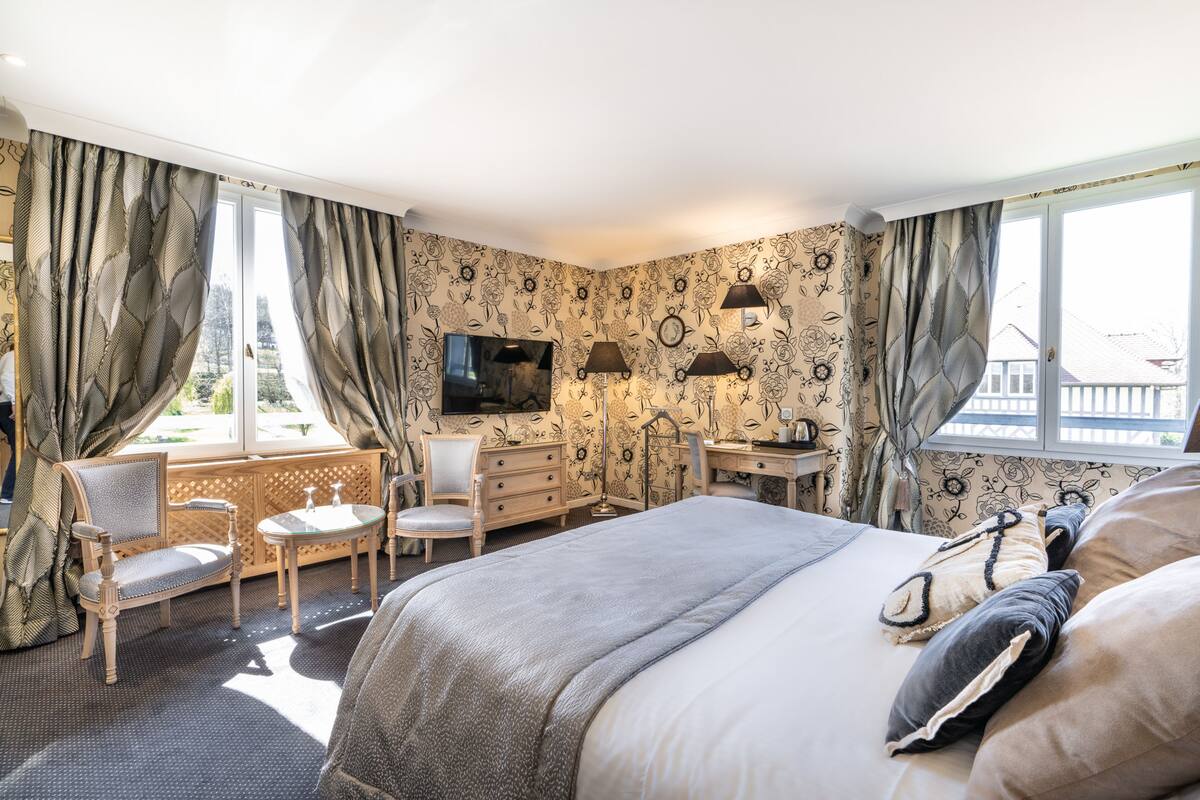 Une chambre d’hôtel avec un lit, un bureau, une chaise, une télévision et une fenêtre avec des rideaux.