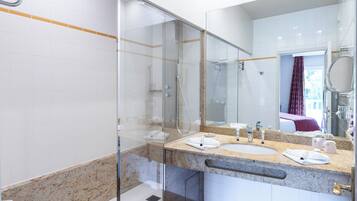 Een moderne badkamer met een glazen douchecabine, twee wastafels en een grote spiegel.