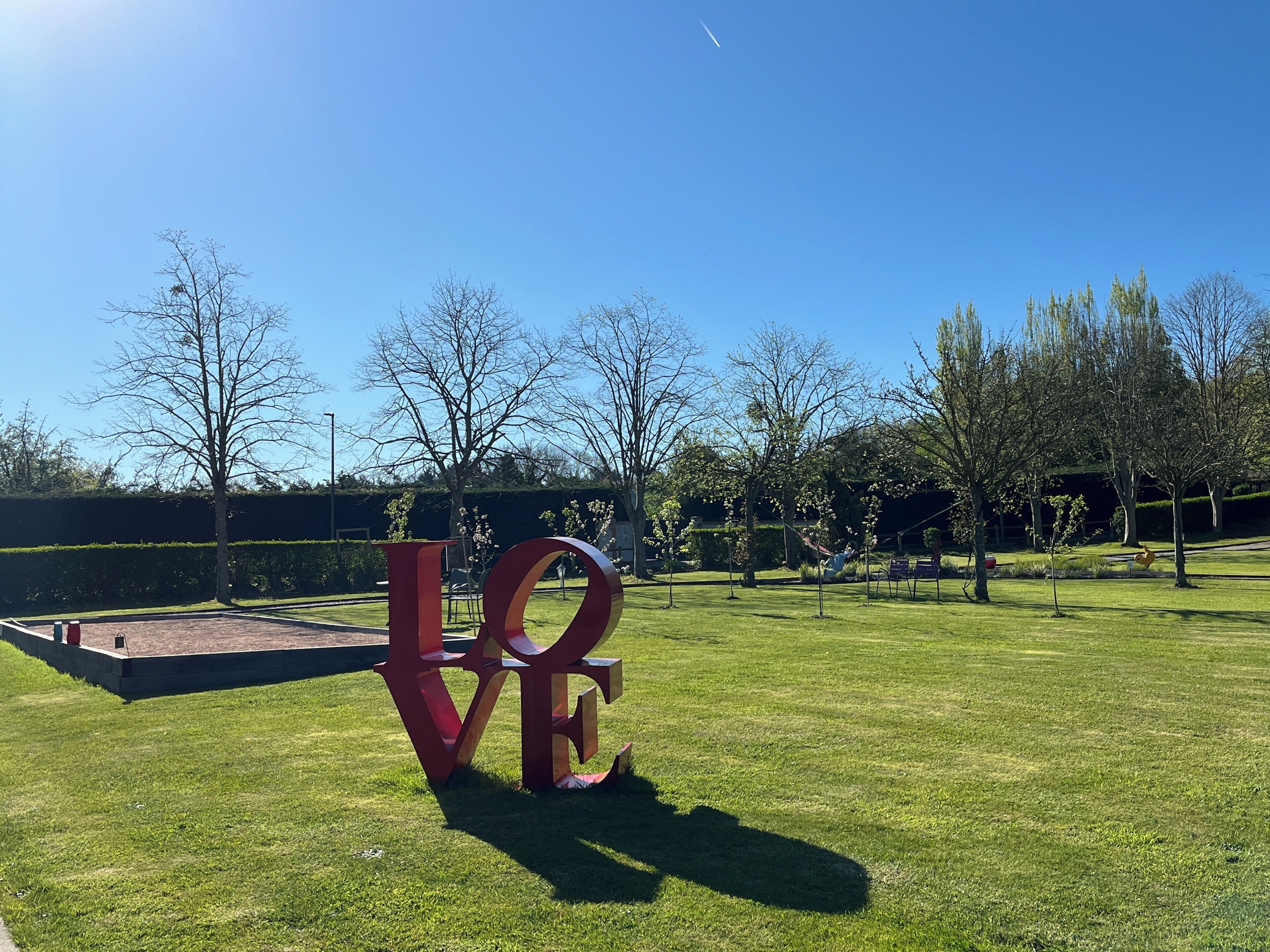 Een grote rode sculptuur met de letters 'LOVE' in een park met gras en bomen.