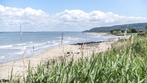 A beach with a sandy shore, grassy foreground, and a view of the sea and distant hills.