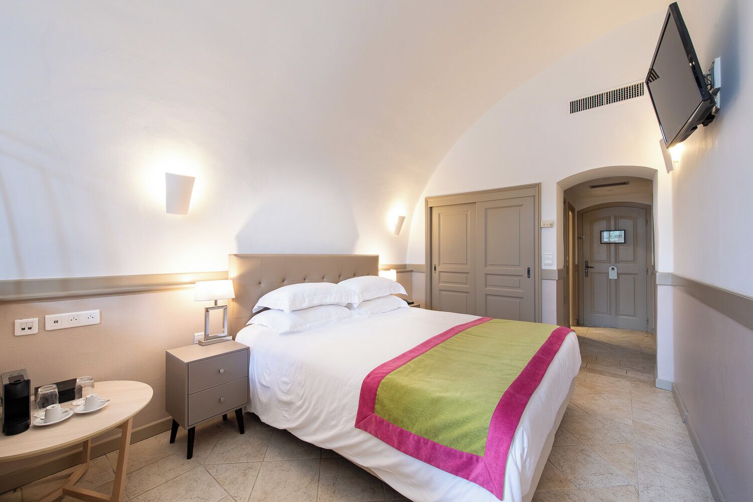 Una camera d'albergo con un letto, un comodino, una lampada e una televisione a parete.