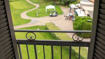 A balcony with a view of a golf course, a tent, and a building with a sloped roof.