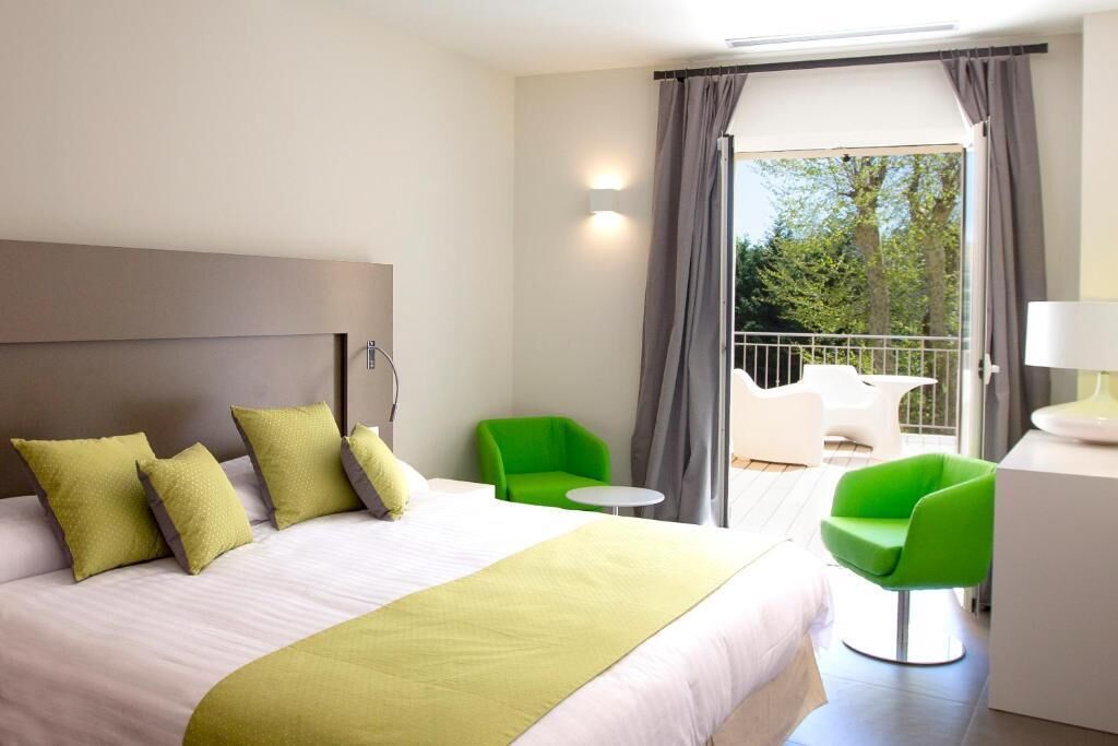 Une chambre d’hôtel avec un lit, des chaises vertes, une petite table et un balcon donnant sur des arbres.