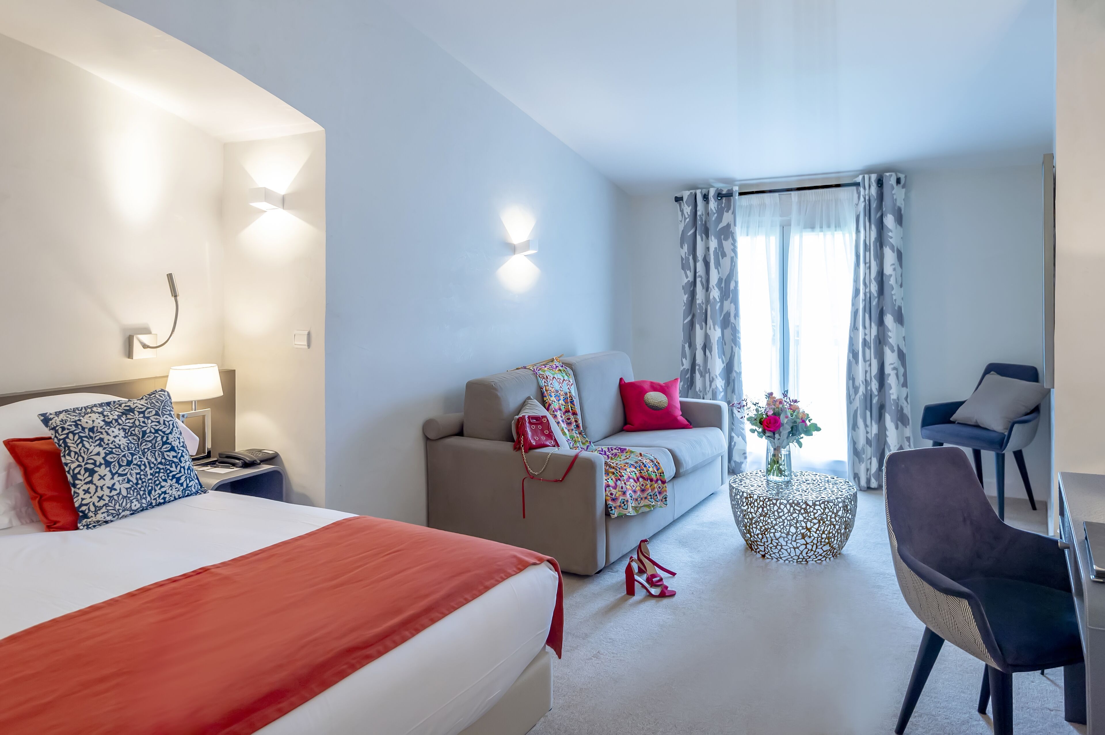 Une chambre d’hôtel avec un lit, un canapé, une chaise, une petite table et une fenêtre avec des rideaux.