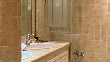 Ein Badezimmer mit beige gefliesten Wänden, einem doppelten Waschbecken, einem Spiegel und einer Badewanne.