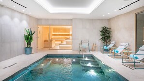Een moderne binnenzwembadruimte met een helder zwembad, ligstoelen en een sauna.