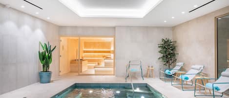 Un área de piscina interior moderna con una piscina cristalina, sillones de descanso y una sala de sauna.