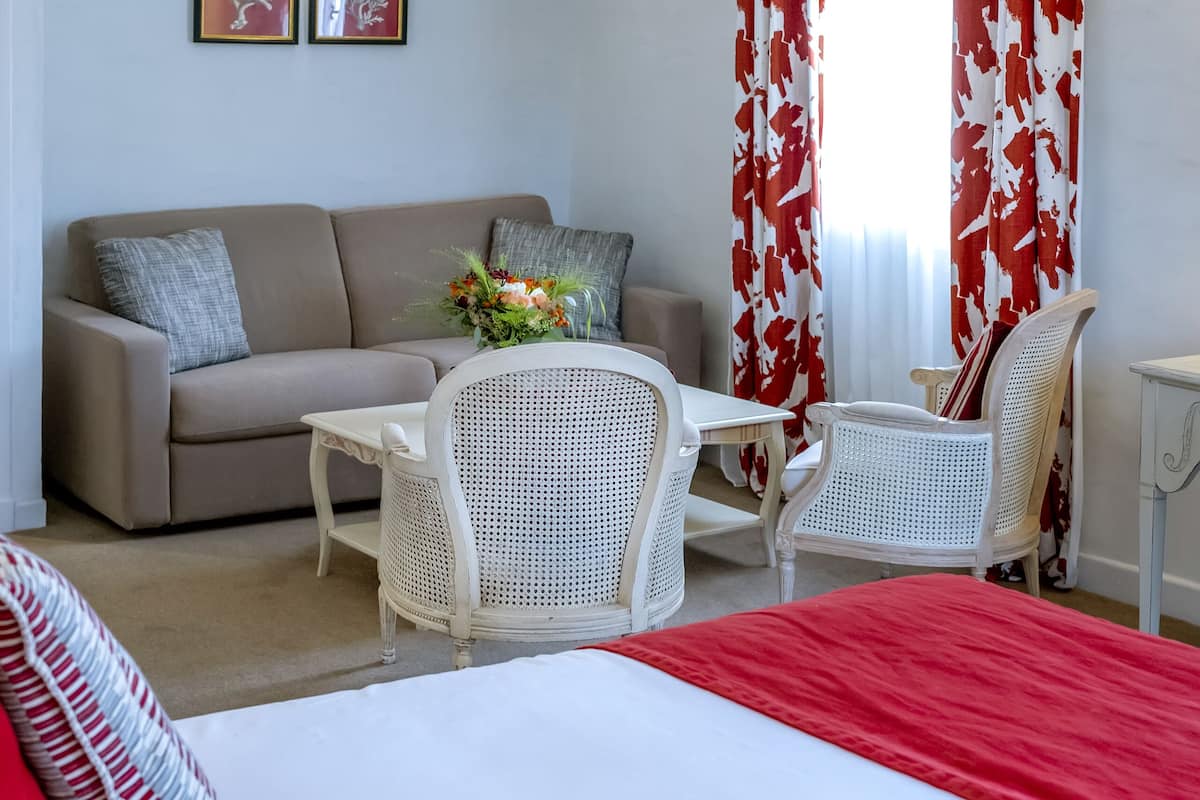 Ein Hotelzimmer mit einem Bett, einer Couch, einem kleinen Tisch, zwei Stühlen und einem Fenster mit Vorhängen.