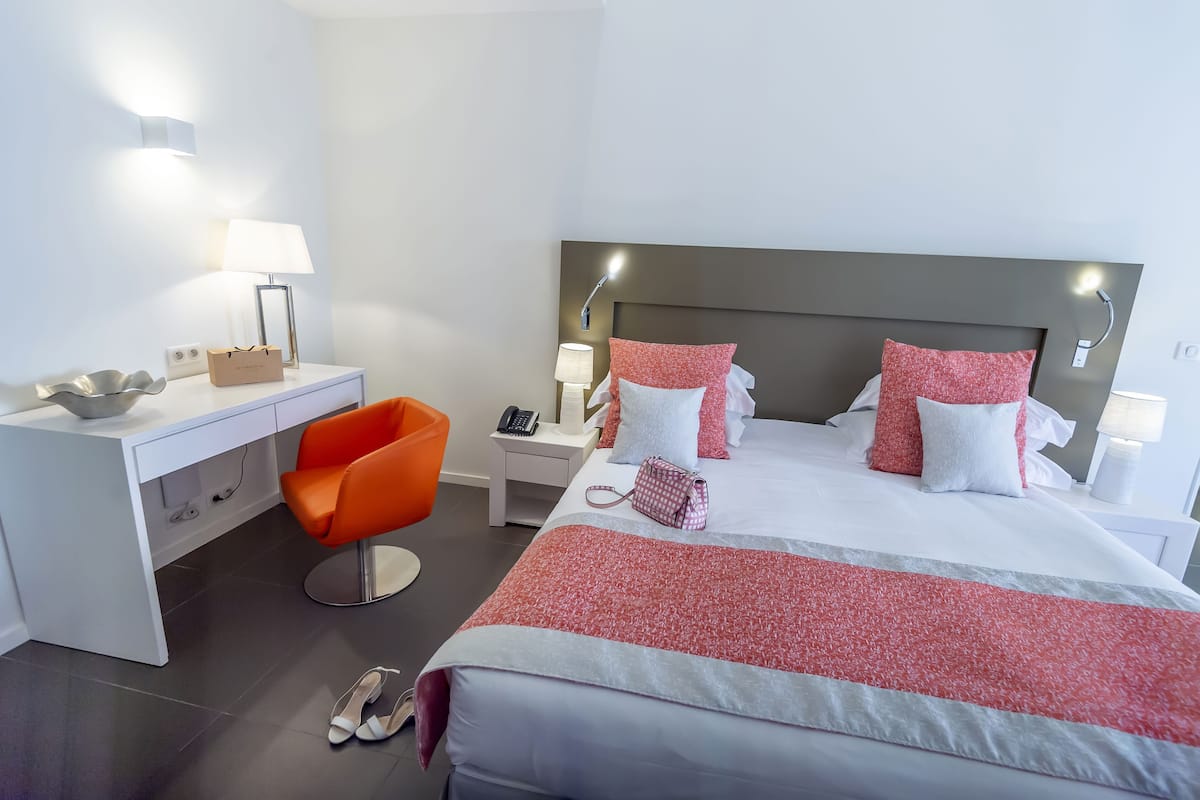 Ein Hotelzimmer mit einem Bett, einem Schreibtisch, einem orangefarbenen Sessel, einem Nachttisch und einer Lampe.