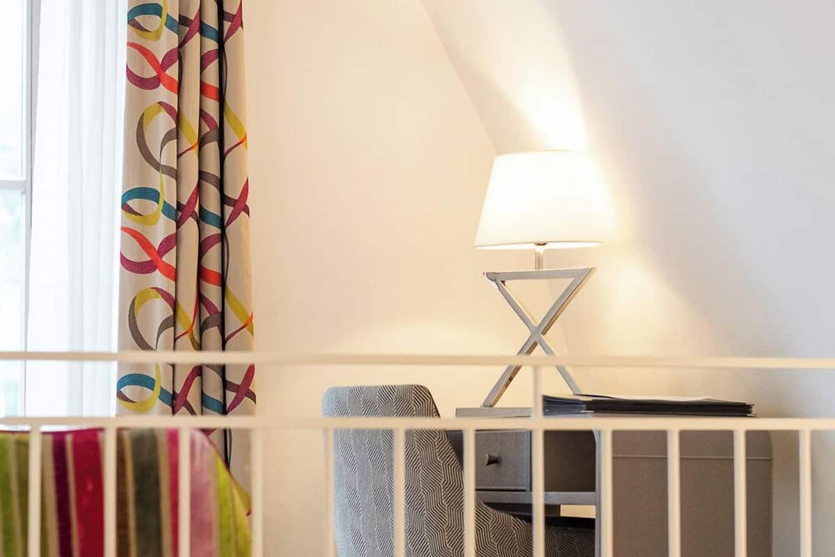 Ein Zimmer mit einem weißen Kinderbett, einem Schreibtisch mit Lampe und einem bunten Vorhang.