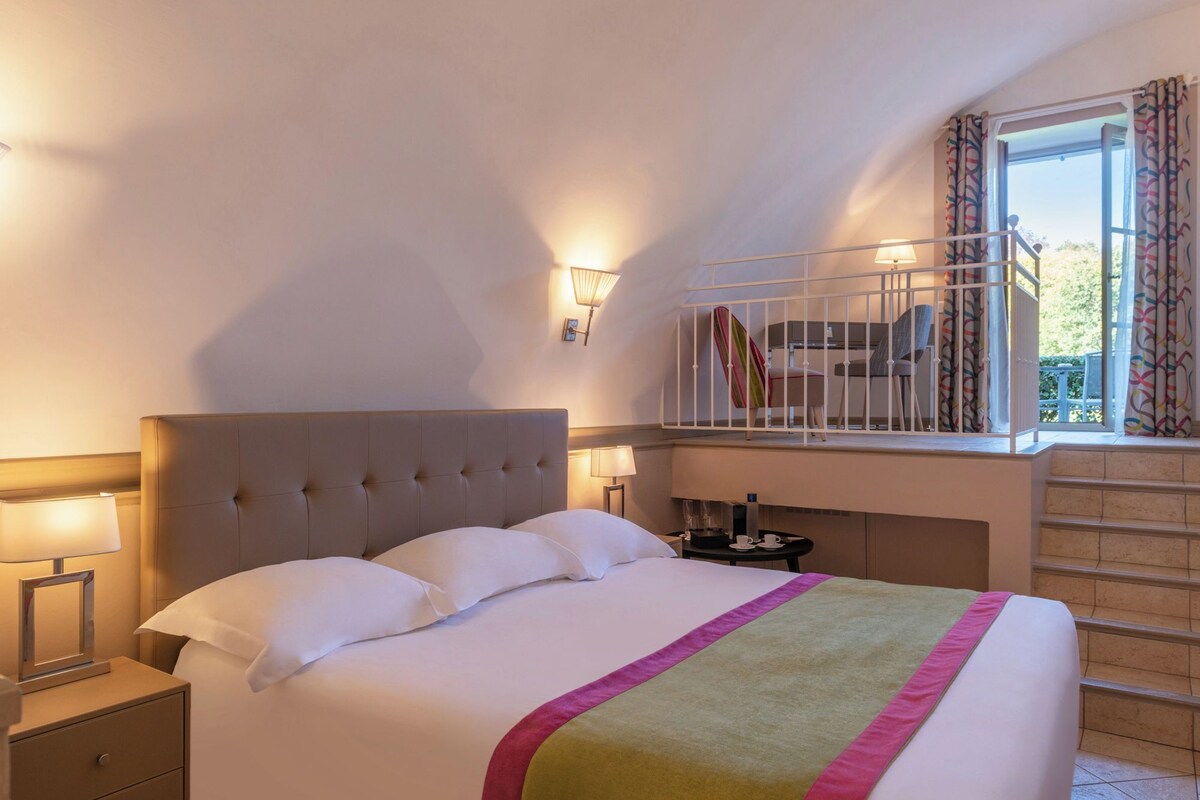 Une chambre d’hôtel avec un grand lit, deux lampes de chevet, une fenêtre avec des rideaux et une vue sur l’extérieur.