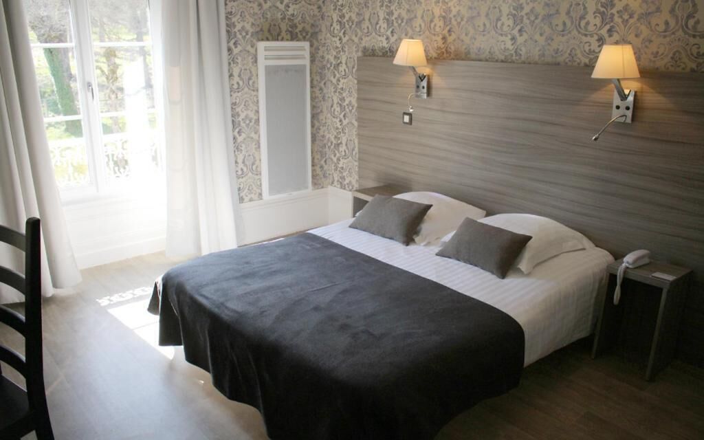A hotel room with a bed, two bedside lamps, a nightstand, a chair, and a window with curtains.
