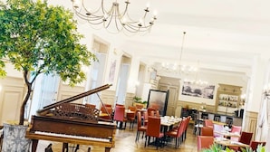 A spacious dining area with a grand piano, elegant chandeliers, and a large tree. - Grand Hôtel de Bourbon-Lancy - Logis - Restaurant et Spa (Bourbon-Lancy)