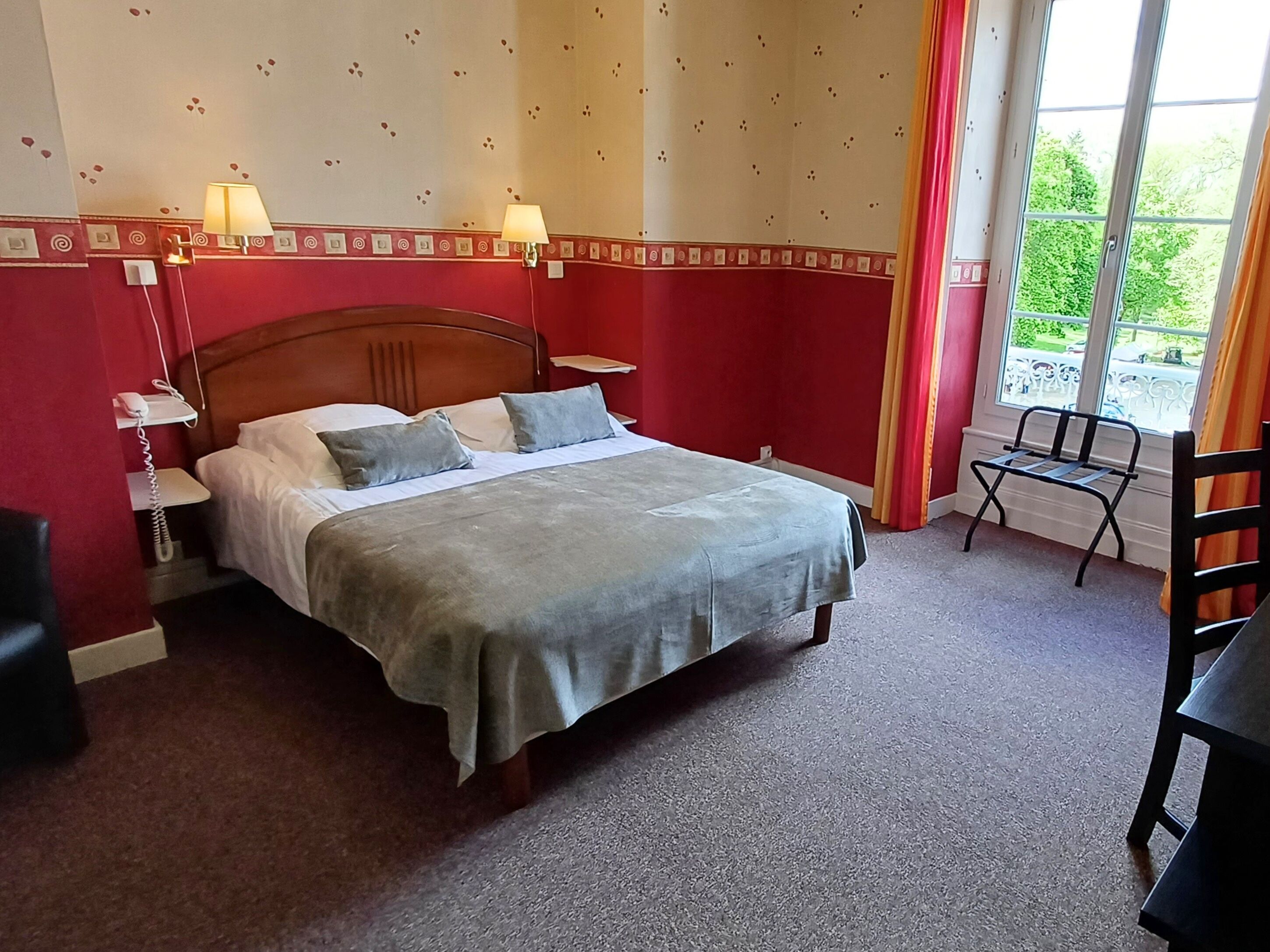 A hotel room with a bed, two bedside lamps, a telephone, a window with curtains, and a chair.