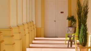 A yellow building with a white door marked with the number 110, a staircase leading to the entrance, and a potted plant beside a green chair. - Grand Hôtel de Bourbon-Lancy - Logis - Restaurant et Spa (Bourbon-Lancy)