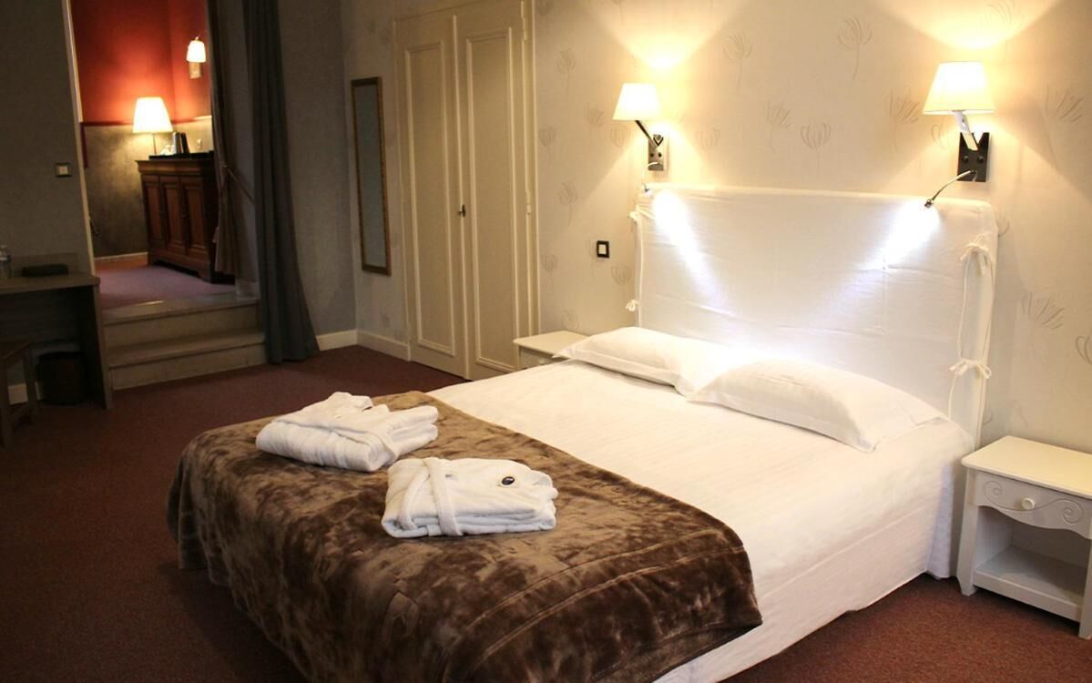A hotel room with a bed, two bedside lamps, a nightstand, a mirror, and a wardrobe.