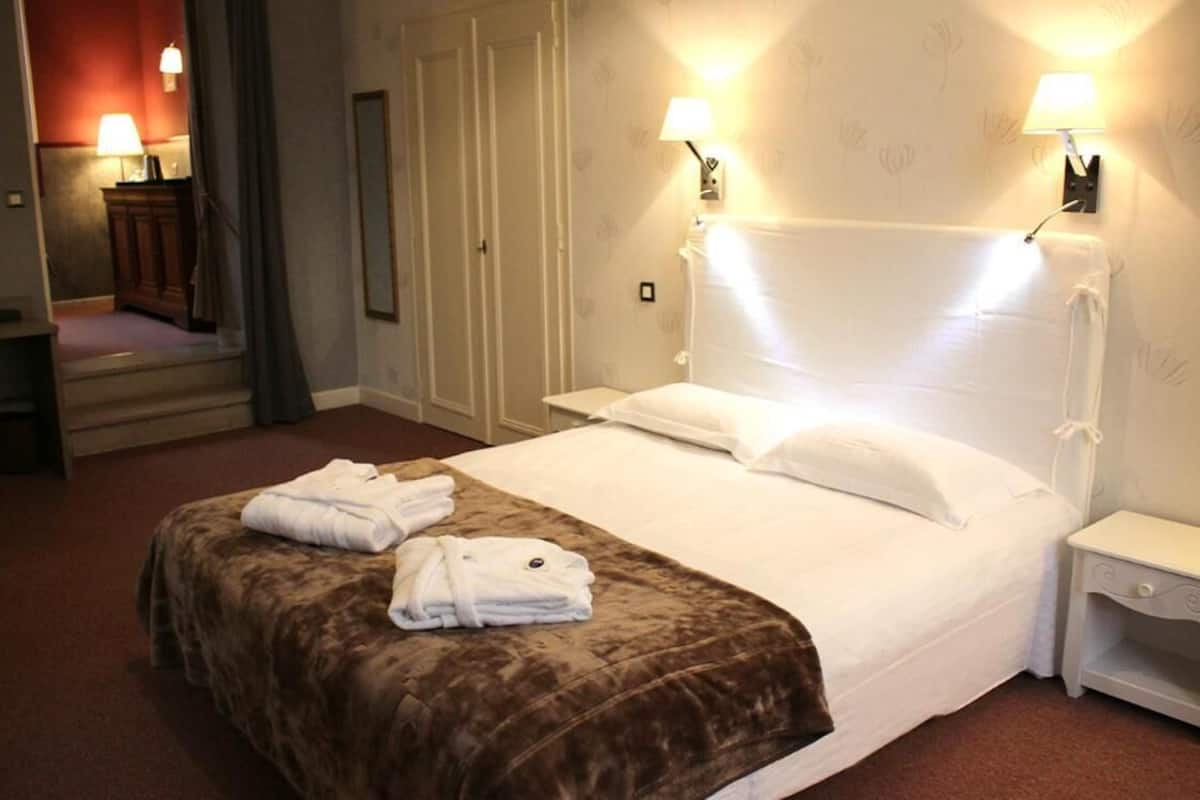 Una habitación de hotel con una cama, dos lámparas de noche, una mesita de noche, un espejo y un armario.