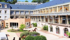 A courtyard with a building featuring multiple balconies, a central garden, and a clear blue sky. - Grand Hôtel de Bourbon-Lancy - Logis - Restaurant et Spa (Bourbon-Lancy)