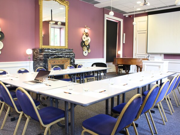 A conference room with a long table, blue chairs, a laptop, and a piano.
