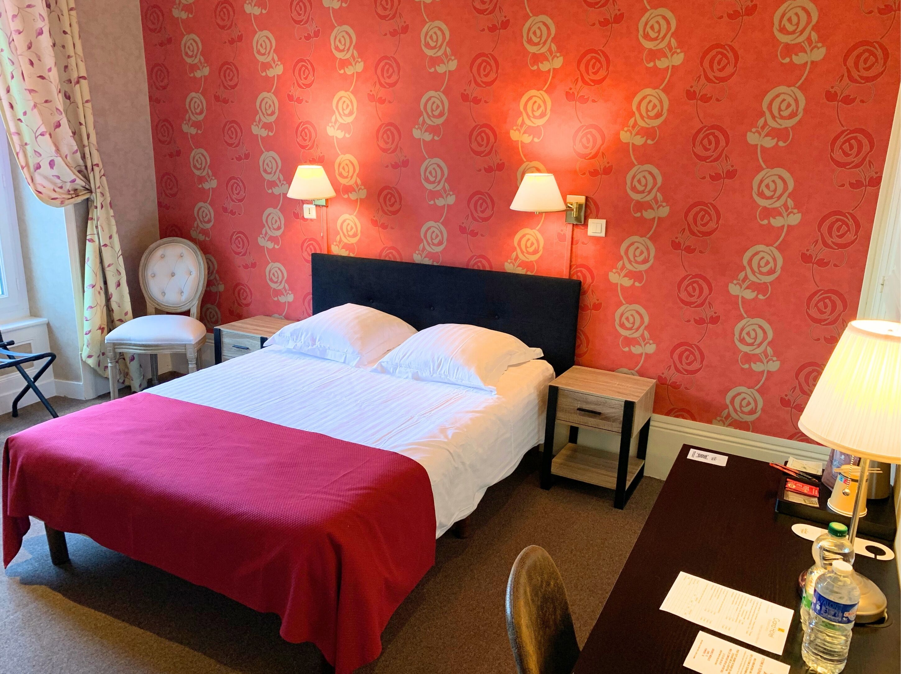 Hotelkamer met een groot bed, twee nachtkastjes, een stoel en een bureau met een lamp en een fles.