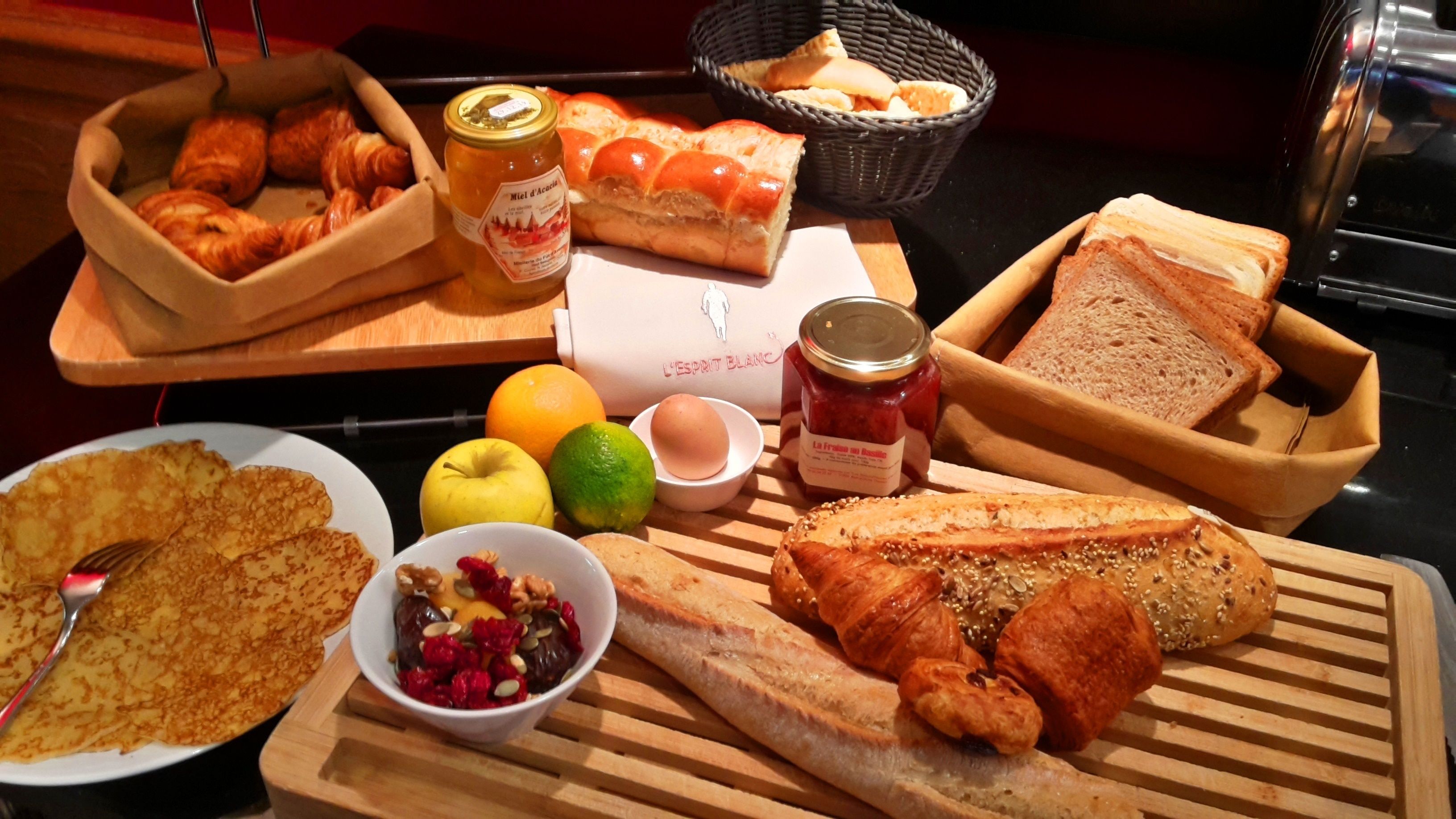 A breakfast buffet with various breads, pastries, fruits, and condiments.