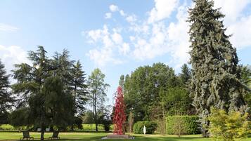 A park with a tall red sculpture, green grass, and large trees.