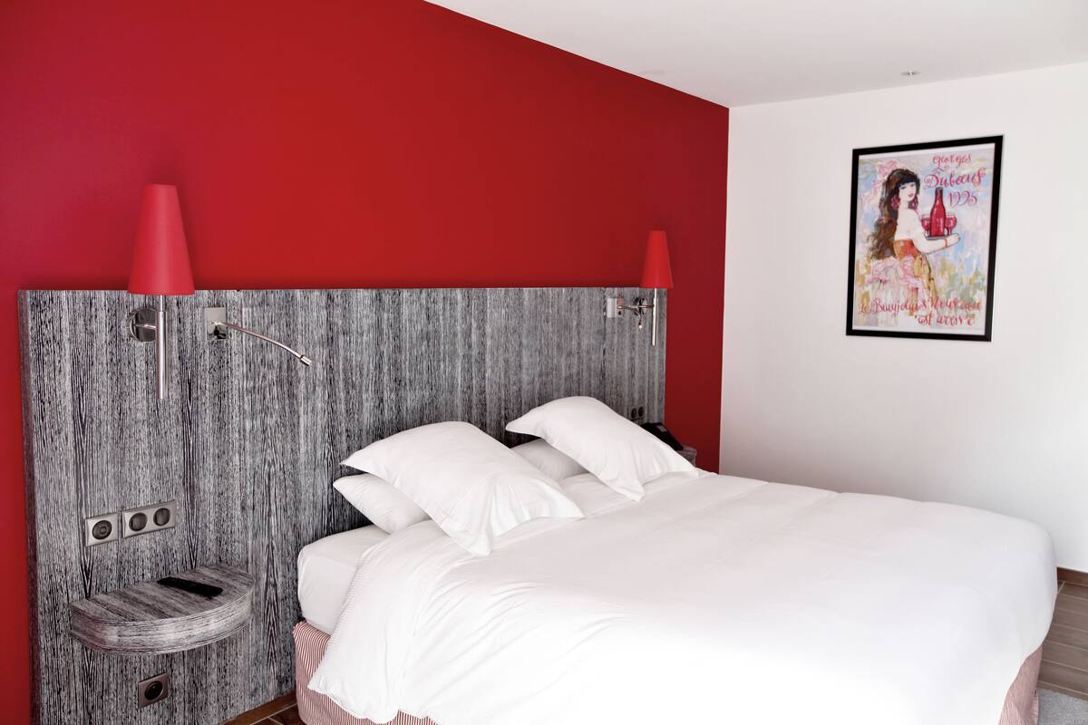 A modern bedroom with a grey textured headboard, white bedding, and red lamps.