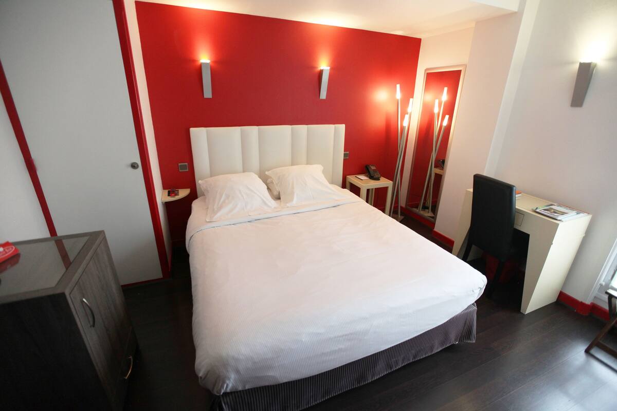A modern hotel room with a large bed, bedside tables, a desk, and a mirror.