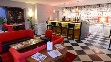 Un vestíbulo de hotel con suelo a cuadros, asientos rojos, una zona de bar y una pared decorativa.