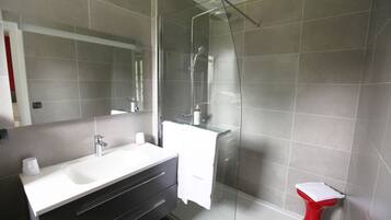 A modern bathroom with a glass-enclosed shower, a white sink, and a red toilet.