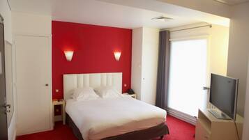 Habitación de hotel con pared de acento roja, una cama grande, televisor y ventana con cortinas.